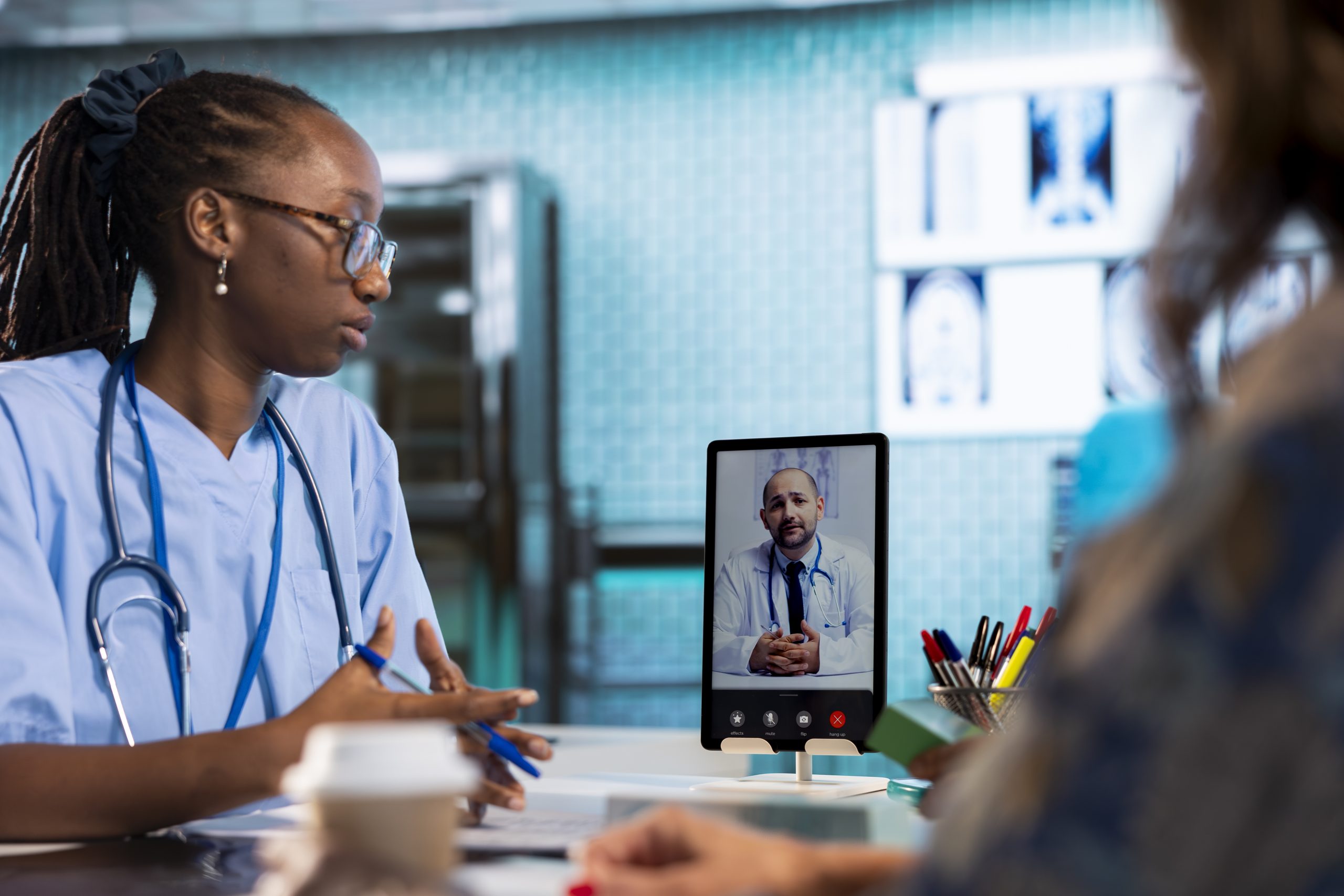 Nurse calling the expert on videoconference to consult two old patients, remote telehealth consultation via internet videocall with specialist. African american assistant offers her support.